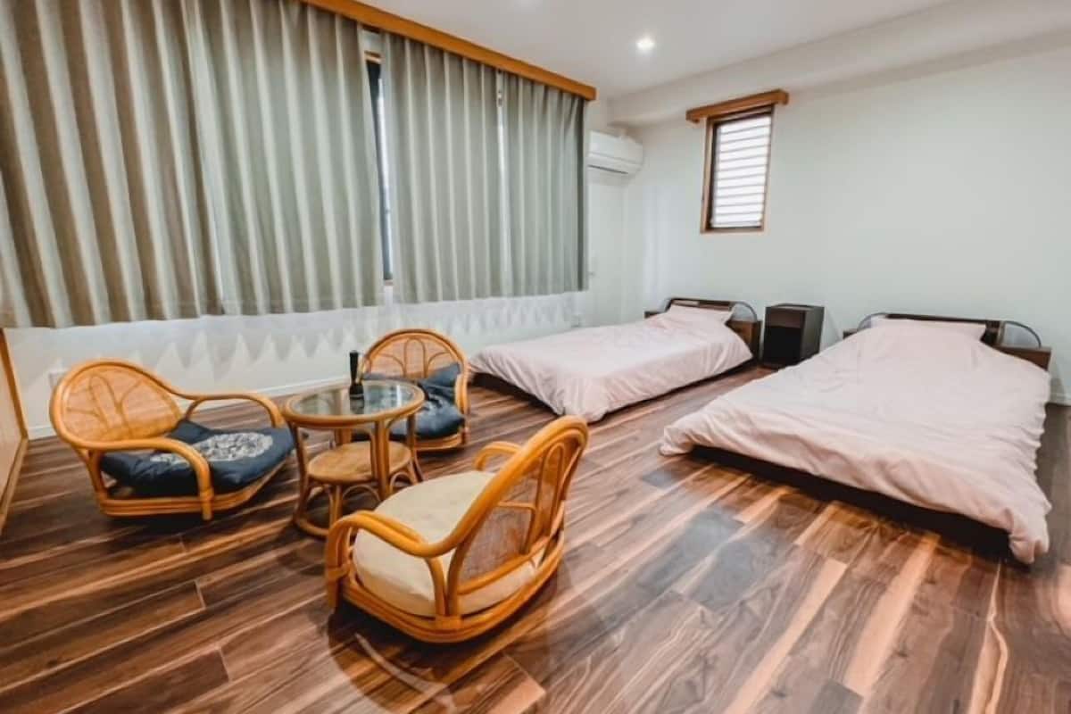 Een hotelkamer met twee eenpersoonsbedden, een klein rond tafeltje met stoelen, en een groot raam met gordijnen.