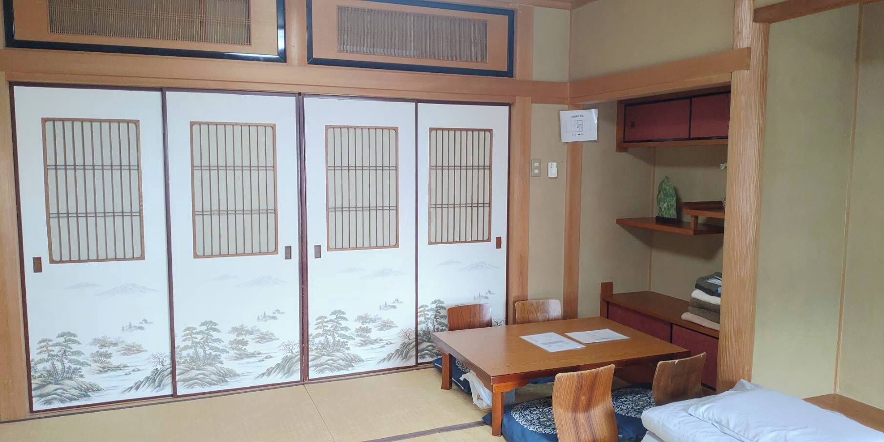 Une pièce traditionnelle japonaise avec un sol recouvert de tatamis, une basse table en bois et une porte coulissante de type shoji ornée d’une peinture représentant un paysage.