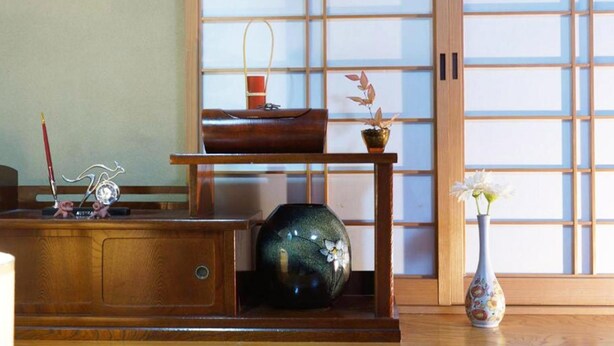 A traditional Japanese room with tatami flooring, a shoji screen, a wooden desk with a vase, and a small table with a potted plant.