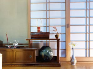 A traditional Japanese room with tatami flooring, a shoji screen, a wooden desk with a vase, and a small table with a potted plant.