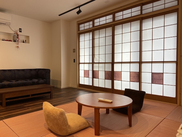 A traditional Japanese room with tatami flooring, a low table, a sofa, and a sliding shoji screen door.