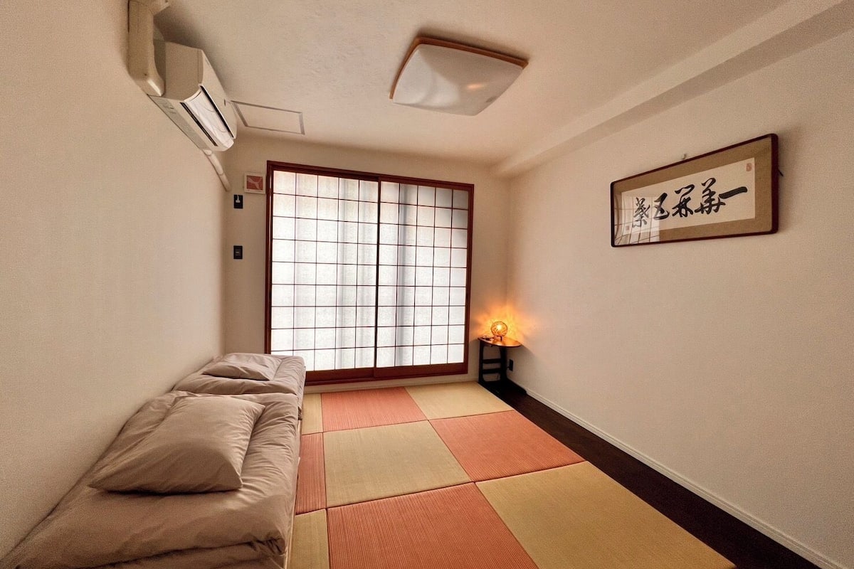 Een kamer met tatami matten, een futonbed, een shoji scherm en een traditionele Japanse lamp.