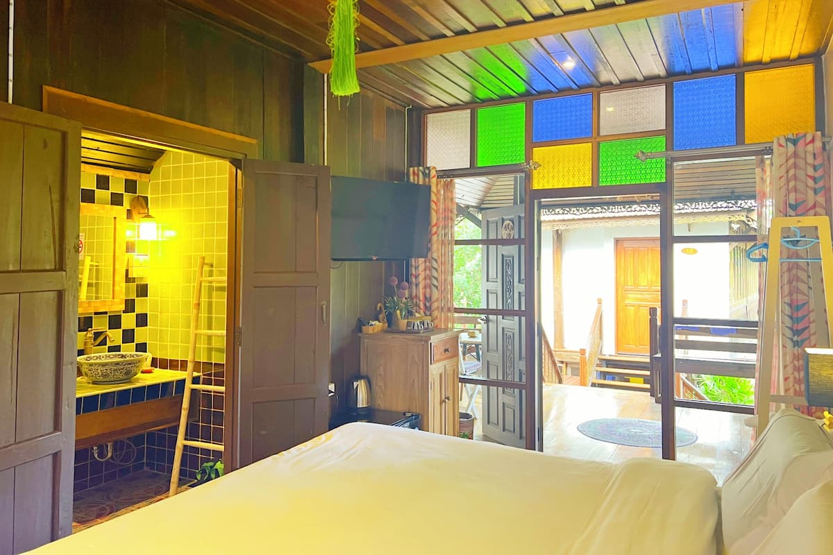 Een kamer met een bed, een houten trap, een betegelde muur en een deur naar een buitenruimte met een tafel en stoelen.