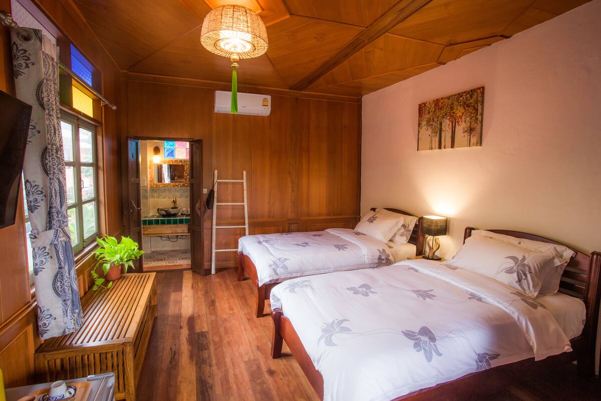 Een kamer met twee bedden, een houten bankje, een tafel, een ladder en een hangende lamp.