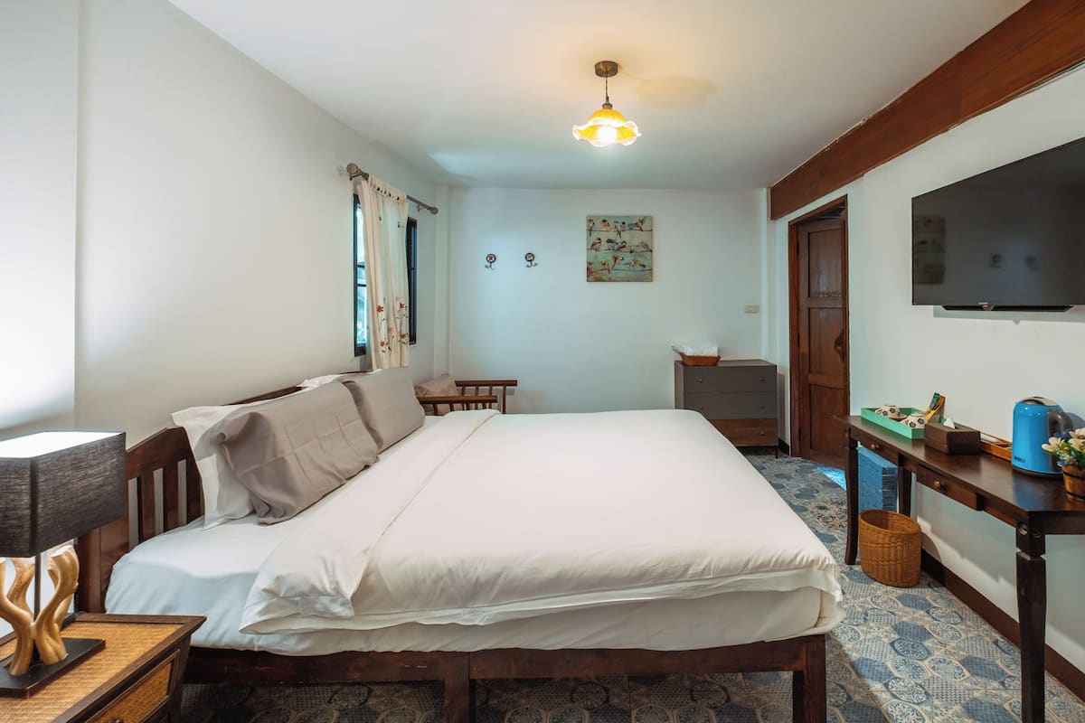 Een netjes ingerichte slaapkamer met een bed, nachtkastje, lamp en een televisie aan de muur.