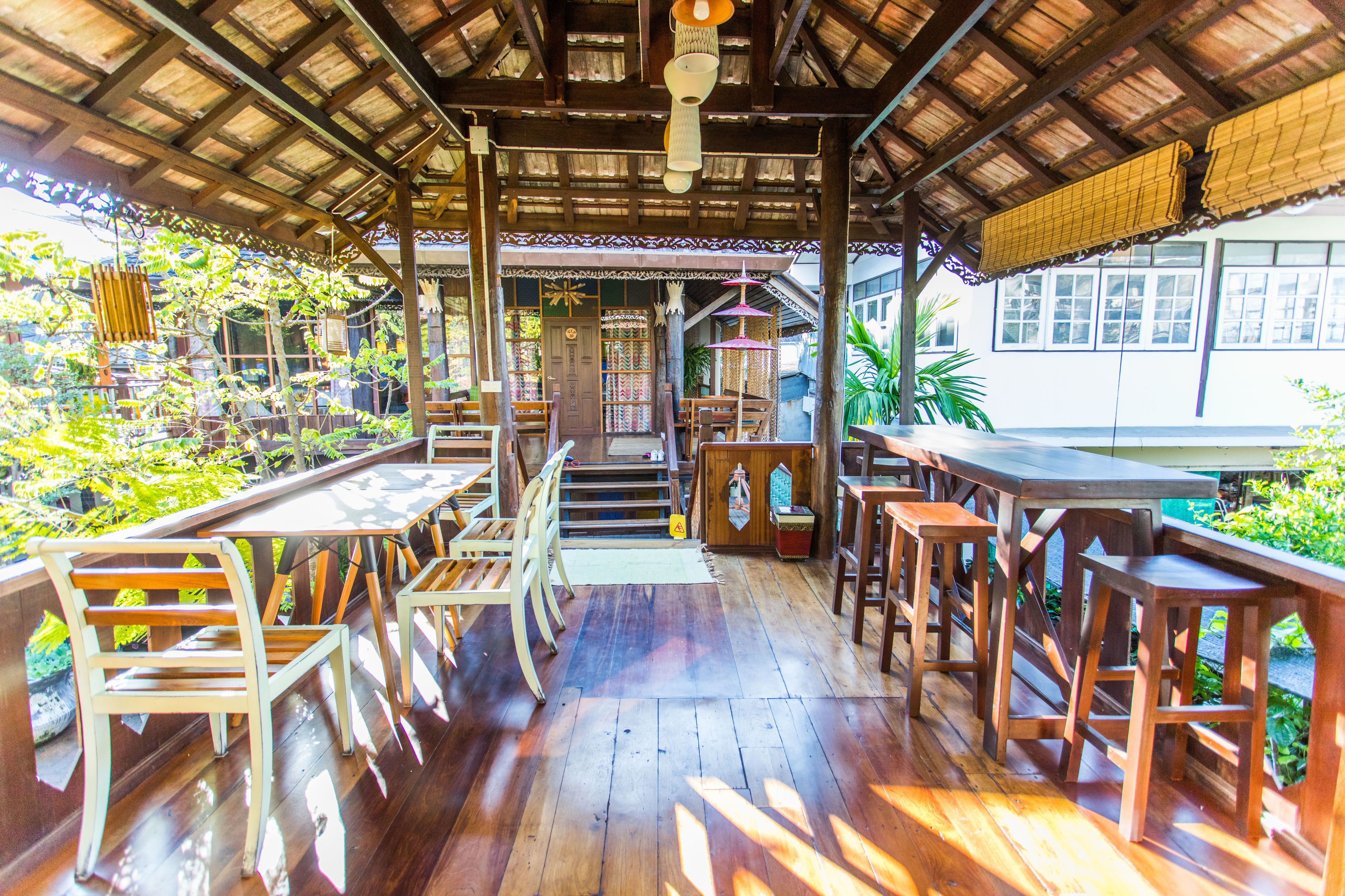 Un espacio comedor al aire libre con techo, mesas y sillas de madera, una escalera que conduce a un nivel superior y vistas de vegetación.