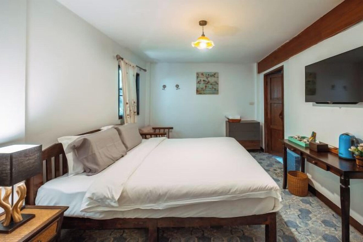 A bedroom with a bed, bedside table, lamp, TV, and a small table with a basket.
