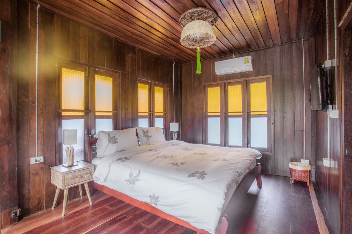 Een houten kamer met een bed, een nachtkastje en een kleine tafel met een lamp.