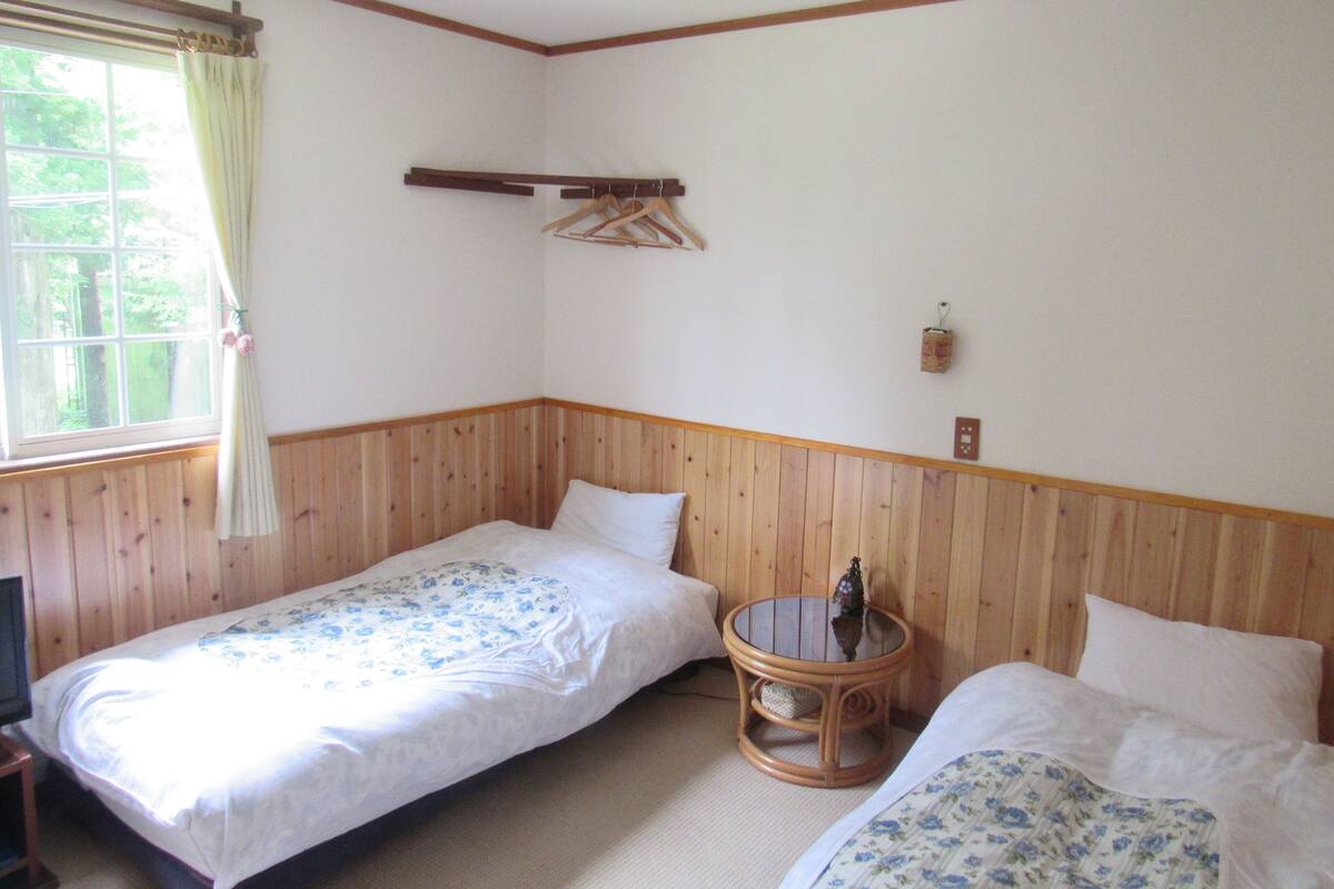 A room with two single beds, a small round table, a TV, and a window with curtains.