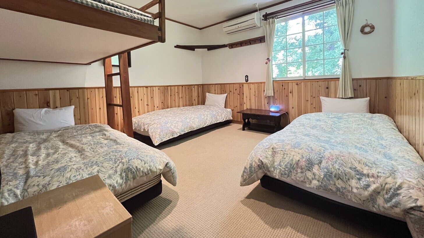 A room with three bunk beds, a small table, and a window with curtains.