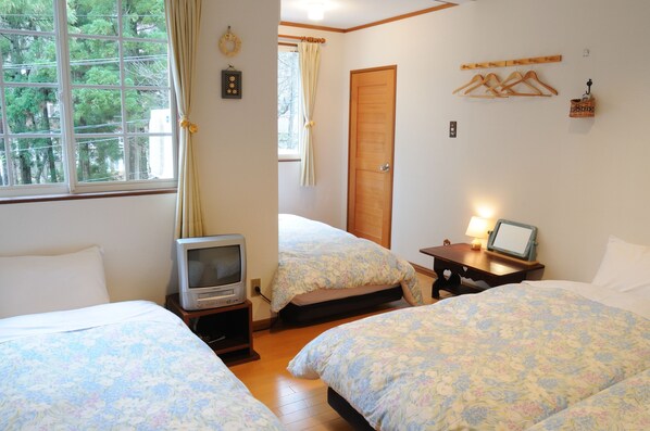 A room with two beds, a television, a window with curtains, and a wooden door.