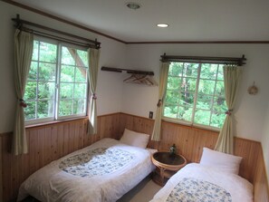 Una habitación con dos camas de madera, una mesita y ventanas con cortinas.
