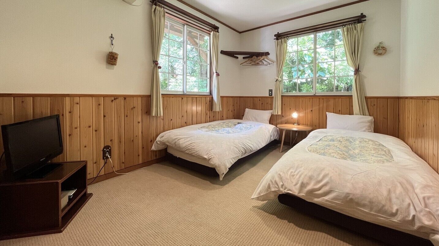 A room with two beds, a television, and windows with curtains.