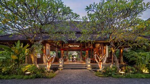 A traditional wooden structure with a tiled roof, surrounded by lush greenery and a cobblestone pathway leading to a central area with a decorative fountain. - The Alantara Sanur (Denpasar)