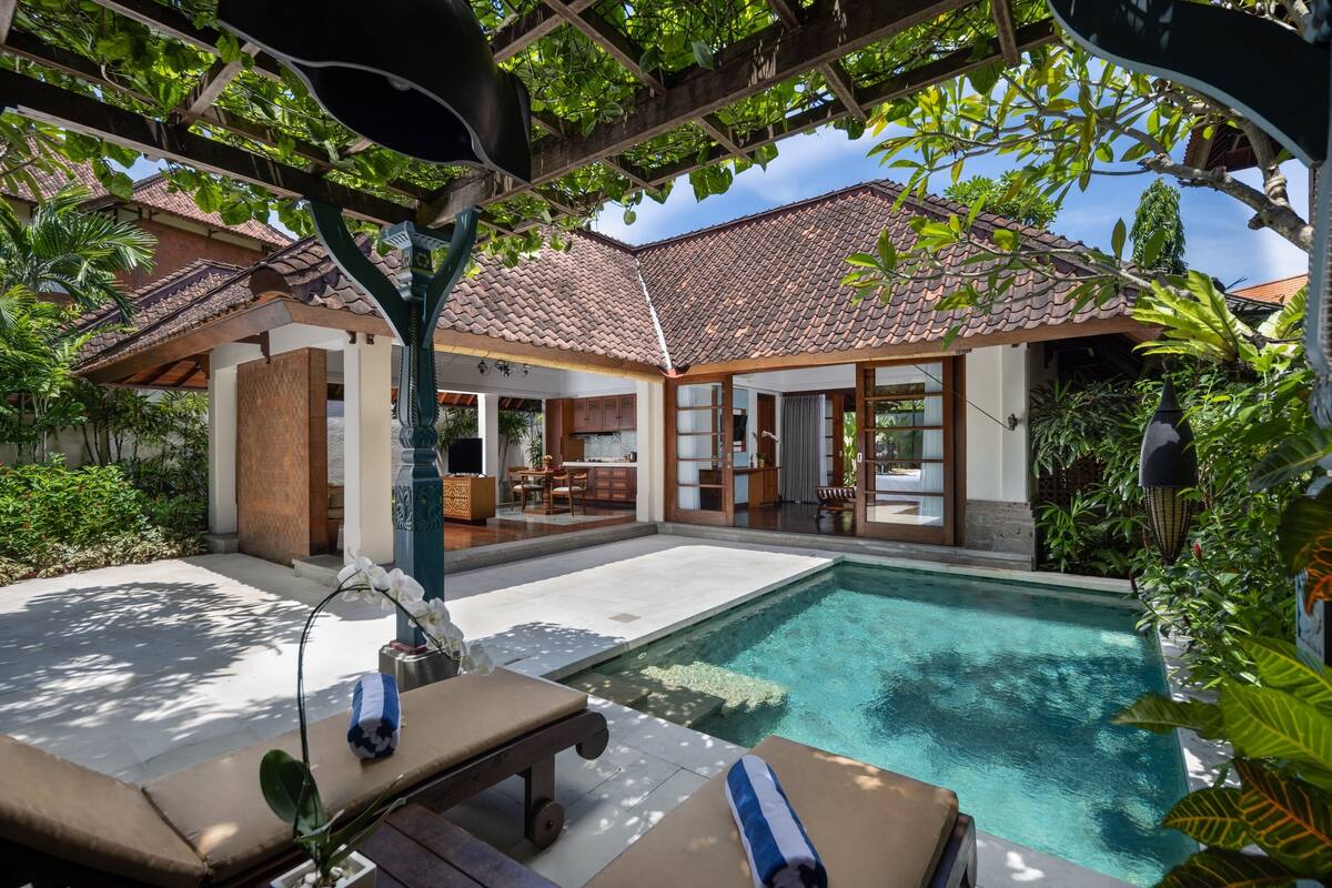 A poolside area with lounge chairs, a tiled deck, and a building with a tiled roof and large windows.