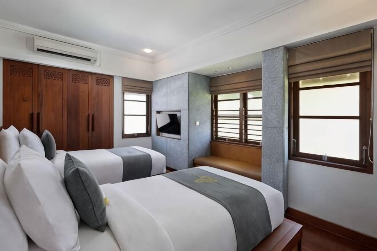 Una habitación de hotel con dos camas, televisión, un ventanal grande y un banco empotrado.