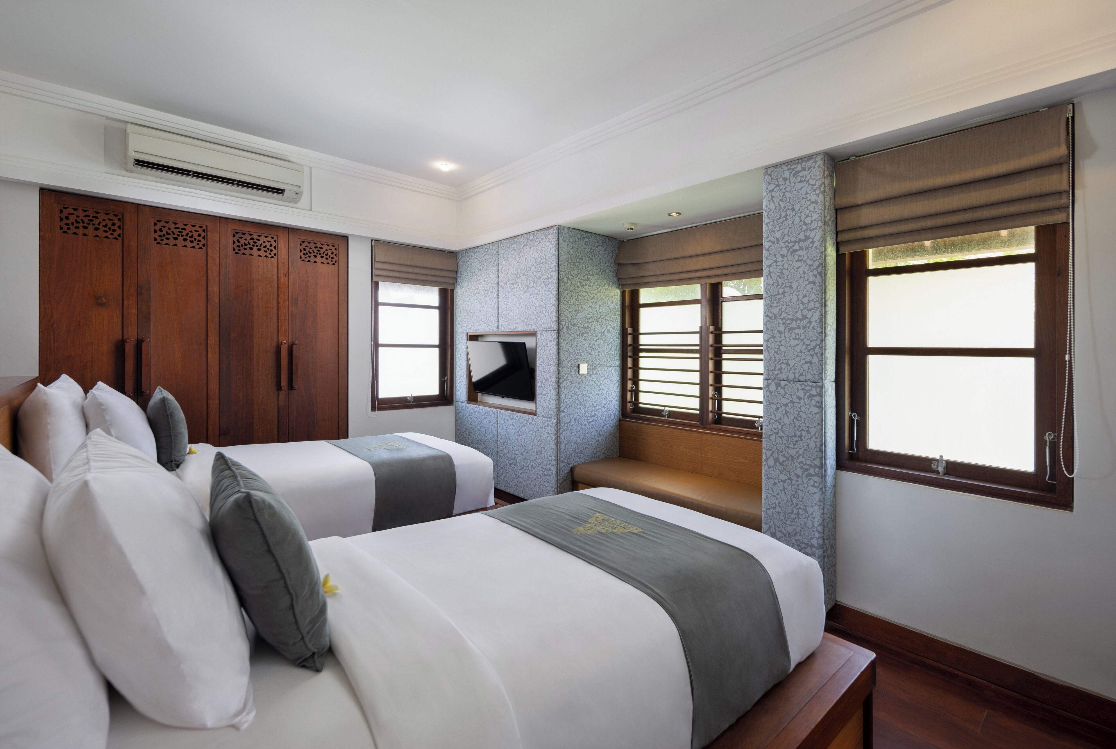 Habitación de hotel con dos camas, televisor, armario y ventanas amplias.