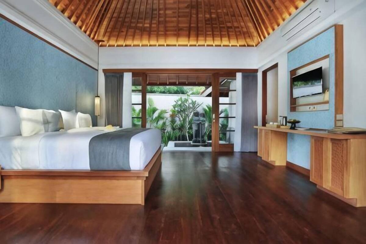 A bedroom with a wooden bed, a TV, and a view of greenery.