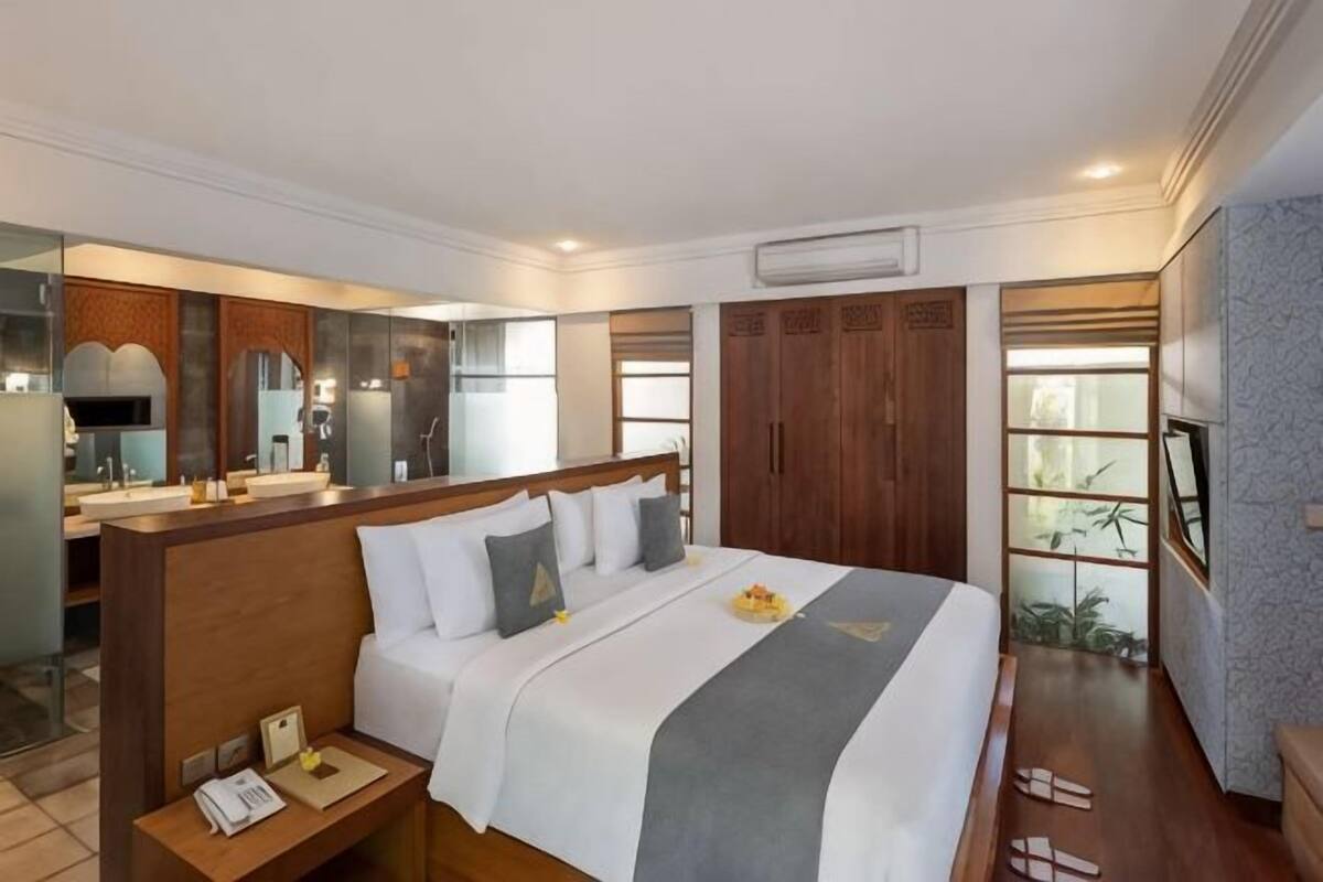 Una habitación de hotel con cama, mesita de noche y baño con espejo y lavabo.