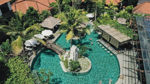 An aerial view of a resort with a central swimming pool, surrounded by palm trees and a small bridge. - The Alantara Sanur (Denpasar)