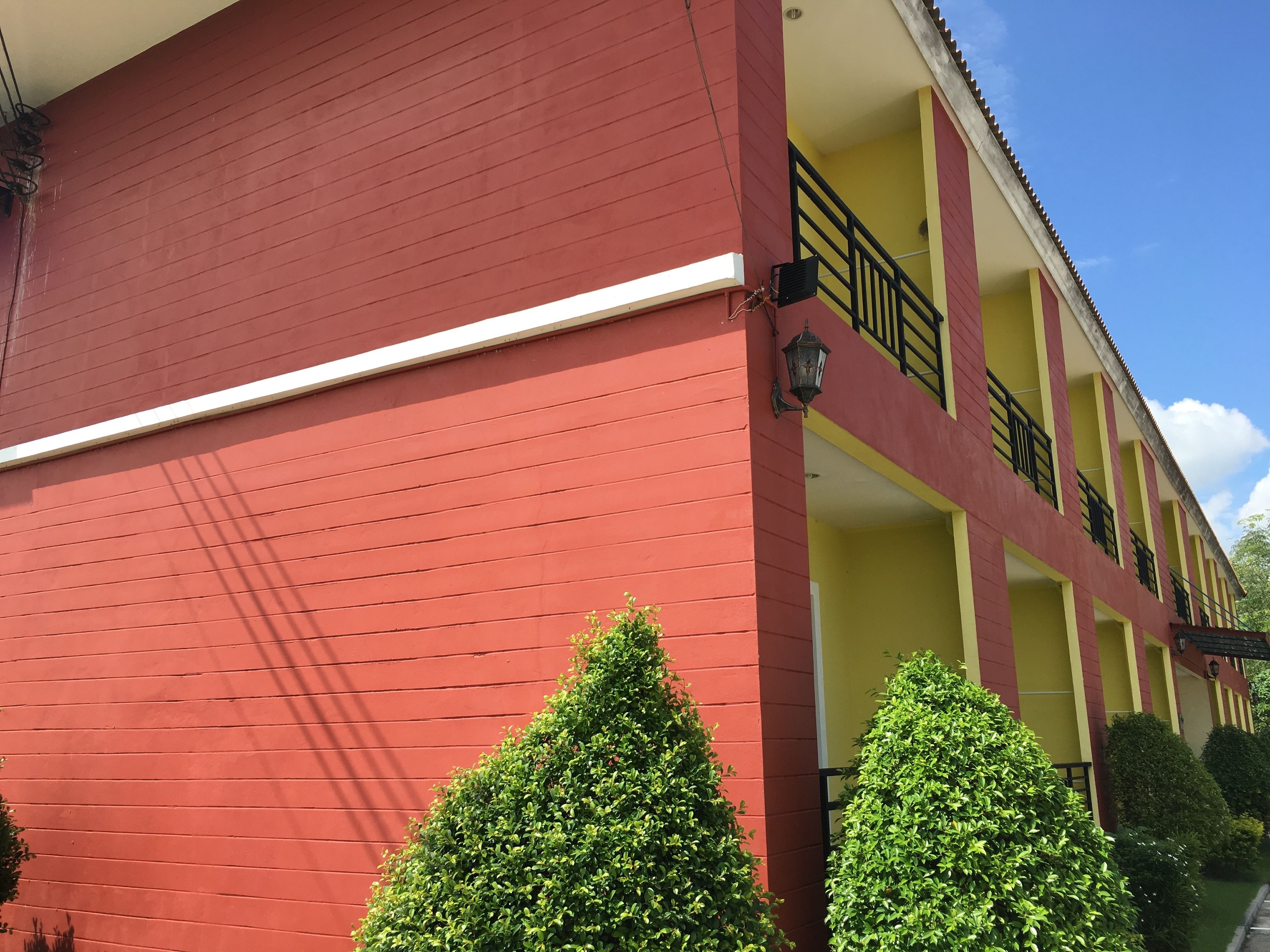 Un bâtiment rouge avec un balcon jaune et des balustrades noires.