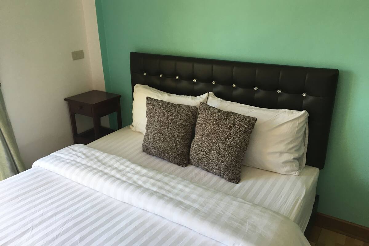 A neatly made bed with a striped bedspread and two pillows, a dark headboard, and a small bedside table.