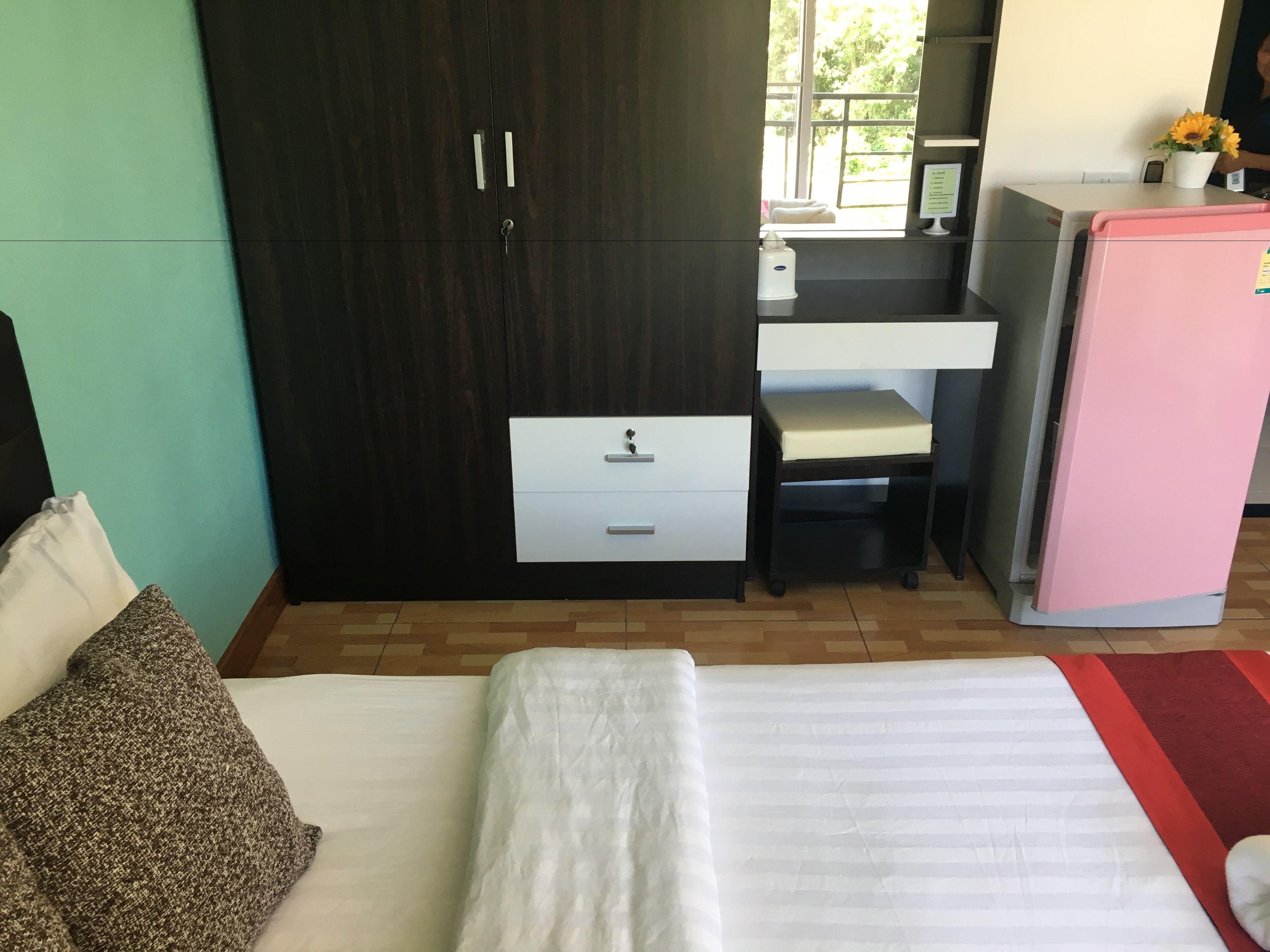 A bedroom with a bed, a desk, a wardrobe, and a refrigerator.