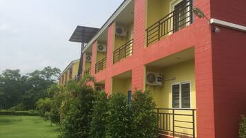 A multi-story building with balconies, air conditioning units, and a green lawn in front.