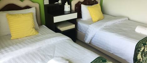 A hotel room with two single beds, each with a white bedspread and a yellow pillow. There is a nightstand with a mirror and a tissue box between the beds.