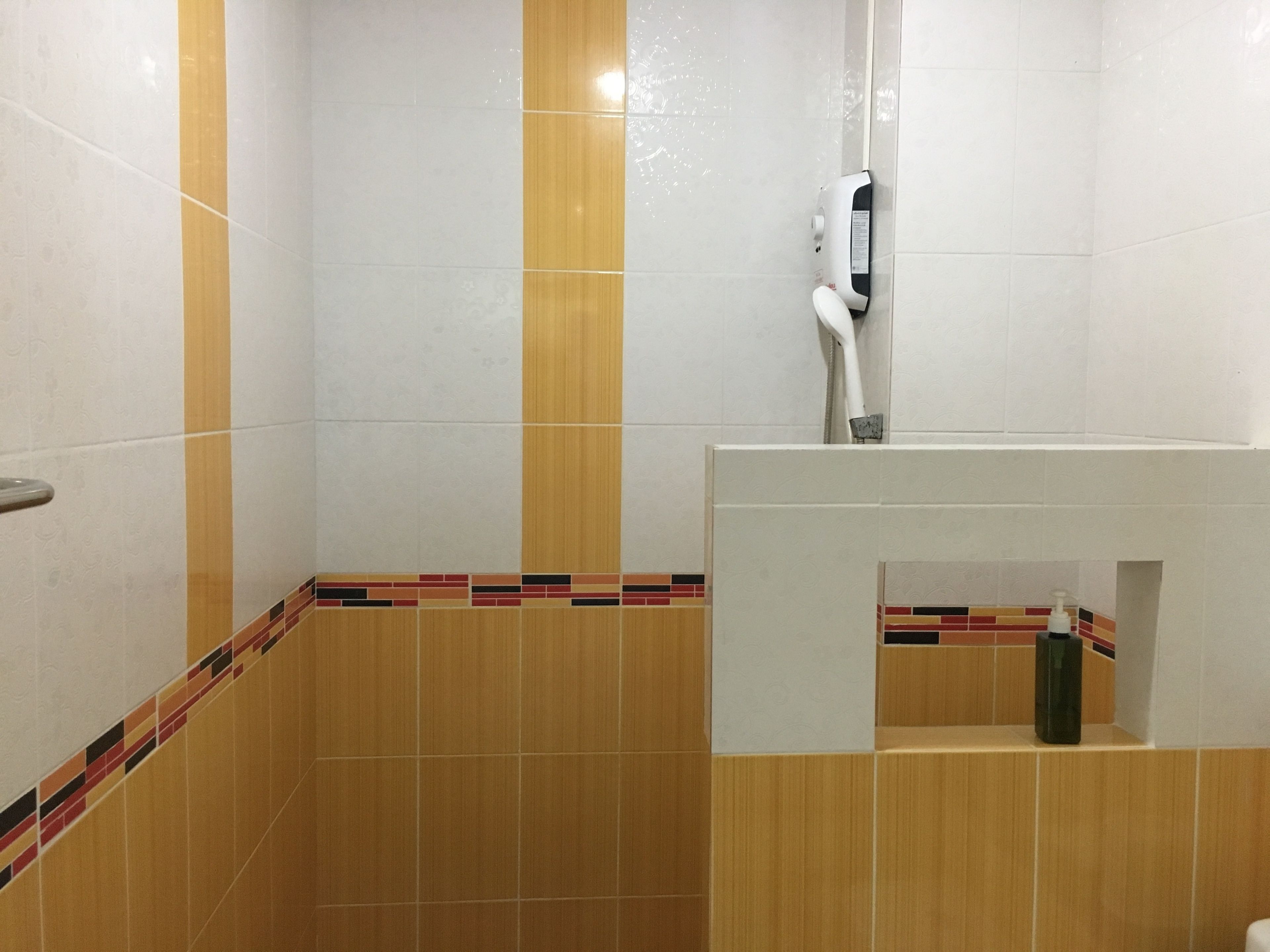 A bathroom with white and wooden tiles, a hand dryer, and a soap dispenser on a shelf.
