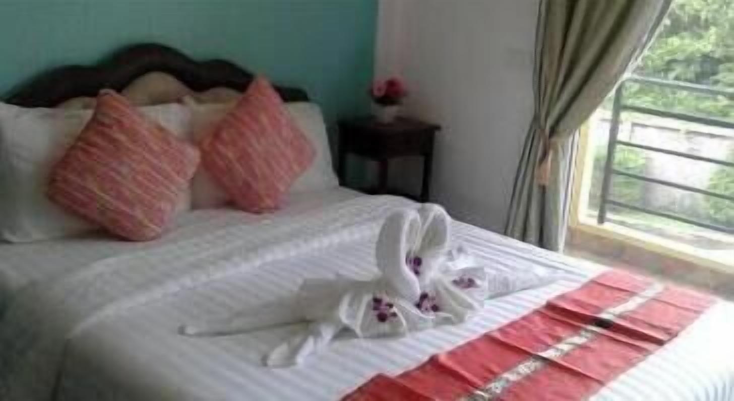 A neatly made bed with pink and white pillows, a white towel, and a red and white striped blanket.
