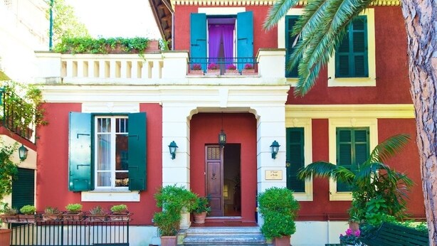 A two-story building with a red facade, green shutters, and a balcony with purple curtains. - Il Tempio di Morfeo (Rome)