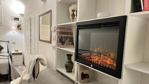 A living room with a flat-screen TV mounted on the wall, a grey sofa, a small table with a lamp, and a bookshelf with various items. - Il Tempio di Morfeo (Rome)