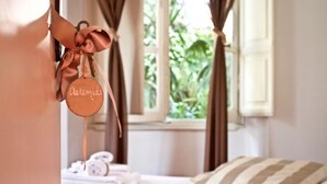 A neatly made bed with a striped pillow, a hanging bathrobe, and a window with curtains. - Il Tempio di Morfeo (Rome)