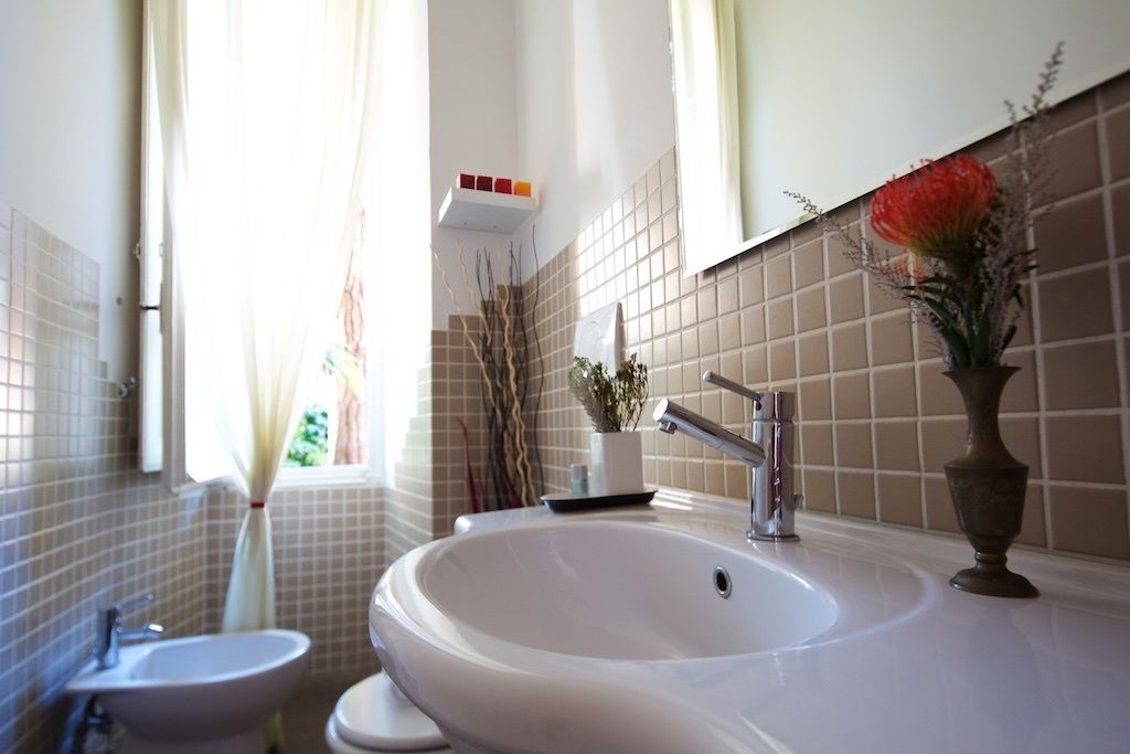 Un baño con un lavamanos grande, un bidé y un inodoro. Hay una ventana con cortinas y una planta en el alféizar.