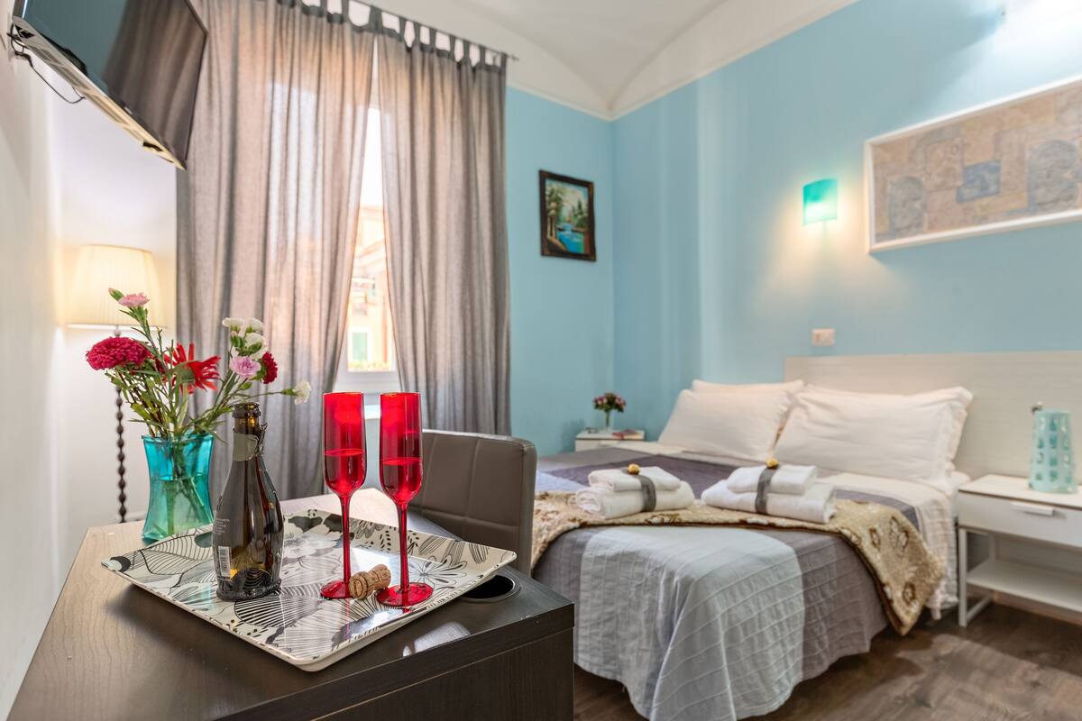 A hotel room with a bed, bedside table, and a window with curtains.