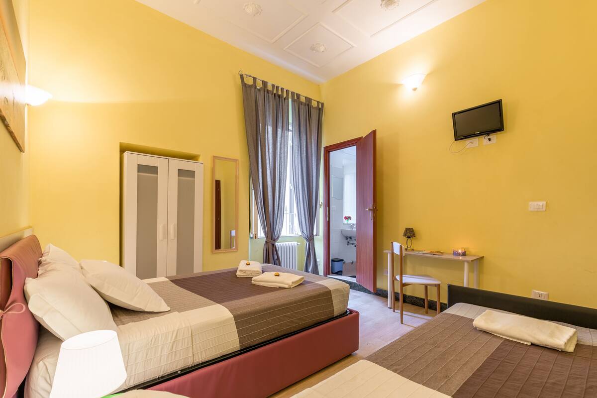 A hotel room with a bed, a desk, a chair, a television, and a bathroom door.