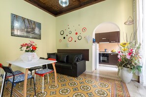 A living room with a sofa, a dining table with chairs, a decorative wall with abstract art, and a kitchen area visible through an archway. - Do Domus (Rome)