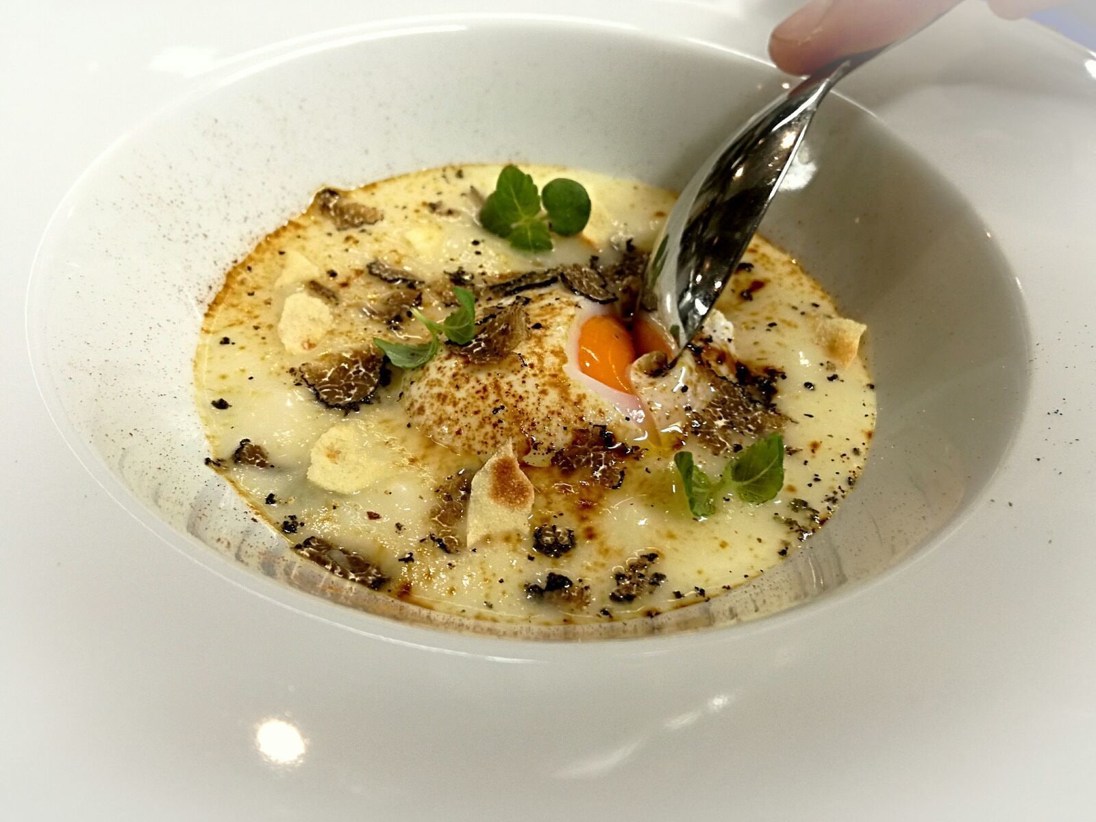 Una ciotola bianca con un cucchiaio, contenente una zuppa cremosa con funghi e erbe aromatiche.