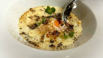 Una ciotola bianca con un cucchiaio, contenente una zuppa cremosa con funghi e erbe aromatiche.