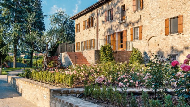 A stone building with a staircase, a garden with pink flowers, and a clear sky. - Borgo Cadonega Relais & SPA (Viano)