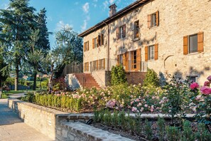A stone building with a balcony, a staircase, and a garden with pink flowers. - Borgo Cadonega Relais & SPA (Viano)