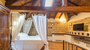 A bedroom with a stone wall, a bed with white bedding, and a TV mounted on the wall. - Borgo Cadonega Relais & SPA (Viano)