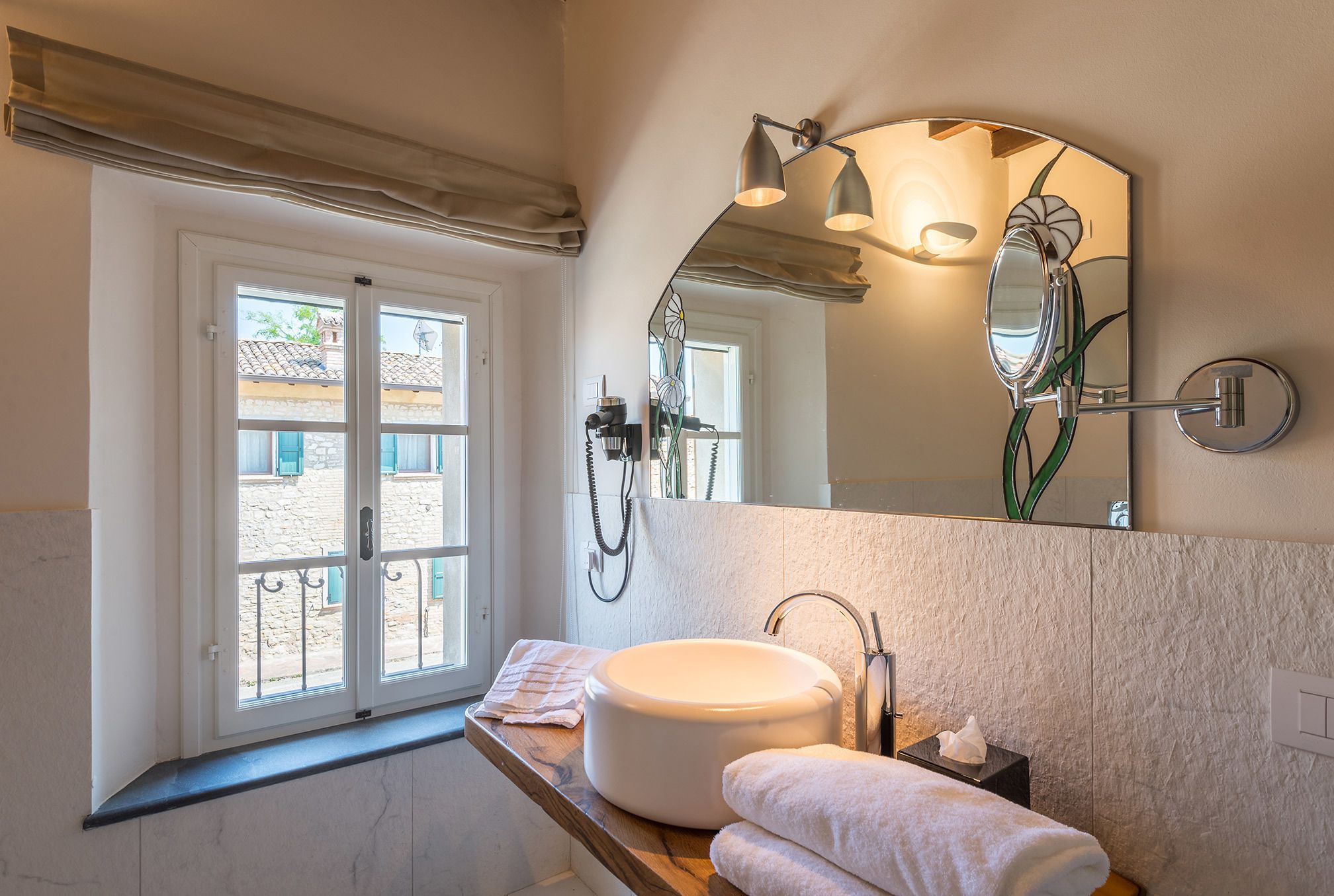 A bathroom with a large window, a round sink, a mirror, and a towel rack.