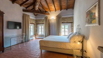A bedroom with a stone wall, wooden beams, a bed, a TV, and a glass table.