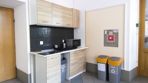 A compact kitchen with a microwave, a small sink, and wooden cabinets. There are two recycling bins and a fire alarm on the wall. - One Lucky Hostel - Old Town (Wroclaw)