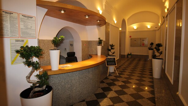 A hotel reception area with a check-in counter, potted plants, and a check-in desk. - One Lucky Hostel - Old Town (Wroclaw)