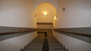 A staircase with granite steps and handrails, leading to a landing with a light fixture and a shield-shaped decoration. - One Lucky Hostel - Old Town (Wroclaw)