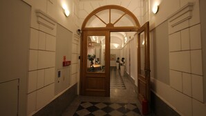 A hallway with a checkered floor, white walls, and a wooden door at the end. - One Lucky Hostel - Old Town (Wroclaw)