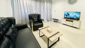 Una sala de estar moderna con un sofá de cuero negro, un sillón capitonado, una mesa de centro de madera y un televisor sobre un mueble de madera.
